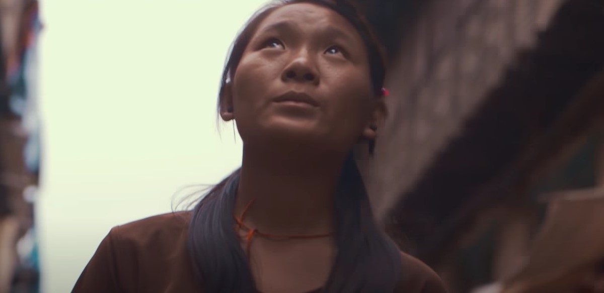 A woman looks up at the sky in a city street.