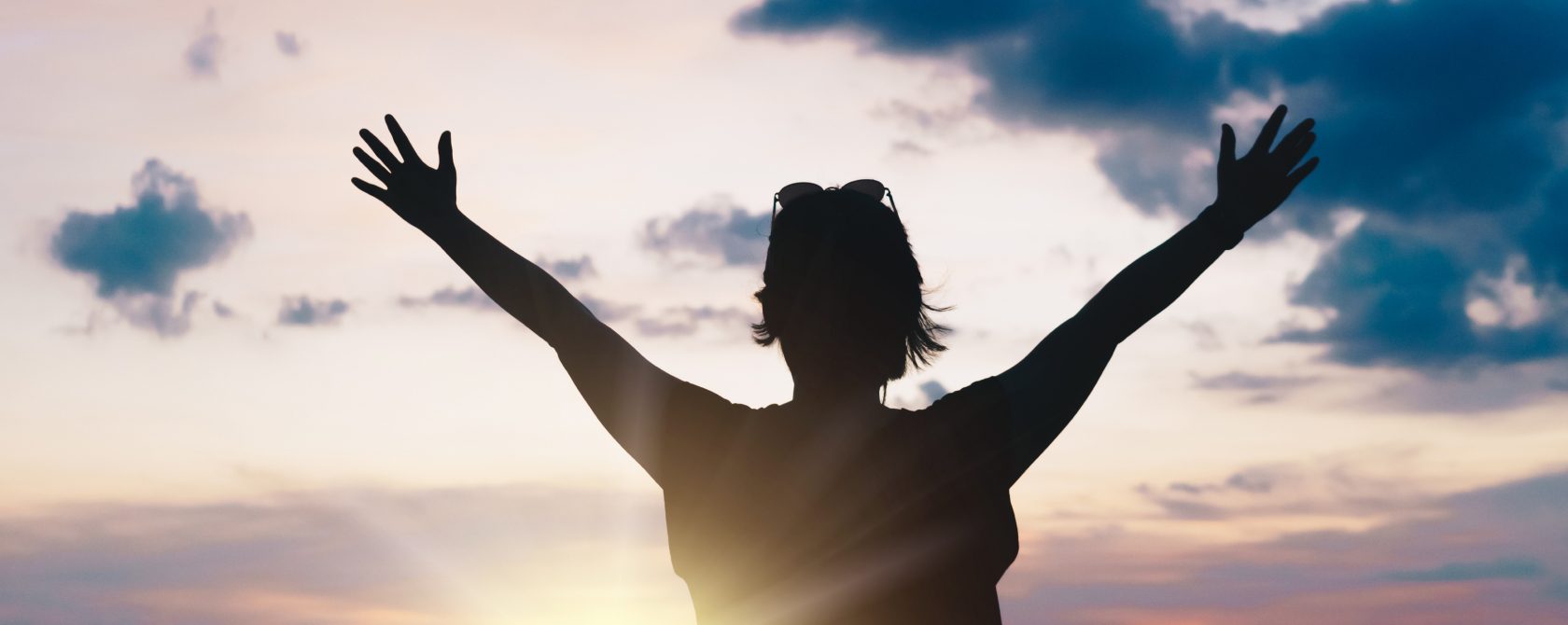 woman raising arms at sunset