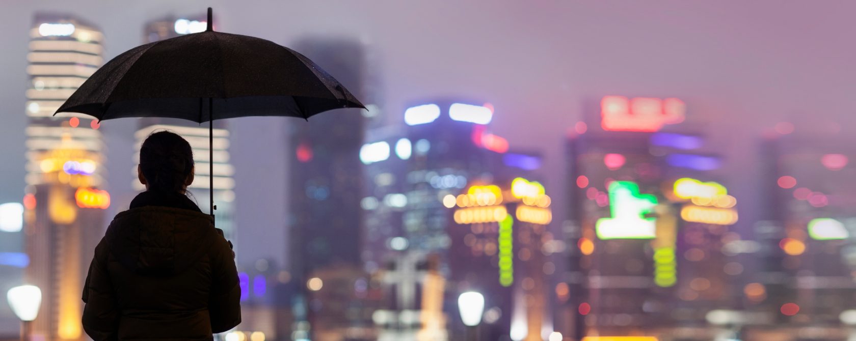 A woman with an umbrella, standing and looking at a city from afar