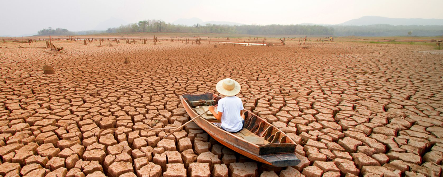 A man on a wooden boat, in the middle of a dry arid land