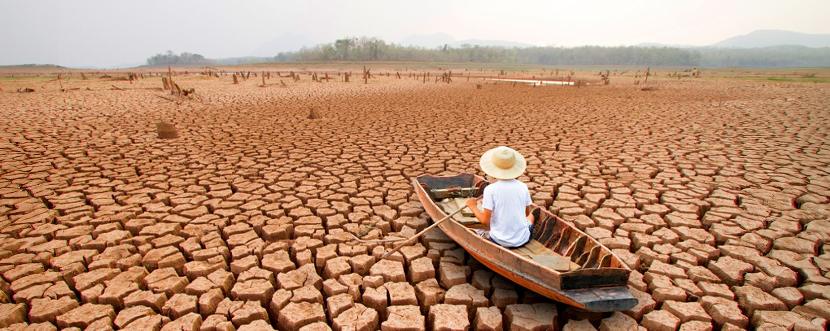 A man on a wooden boat, in the middle of a dry arid land