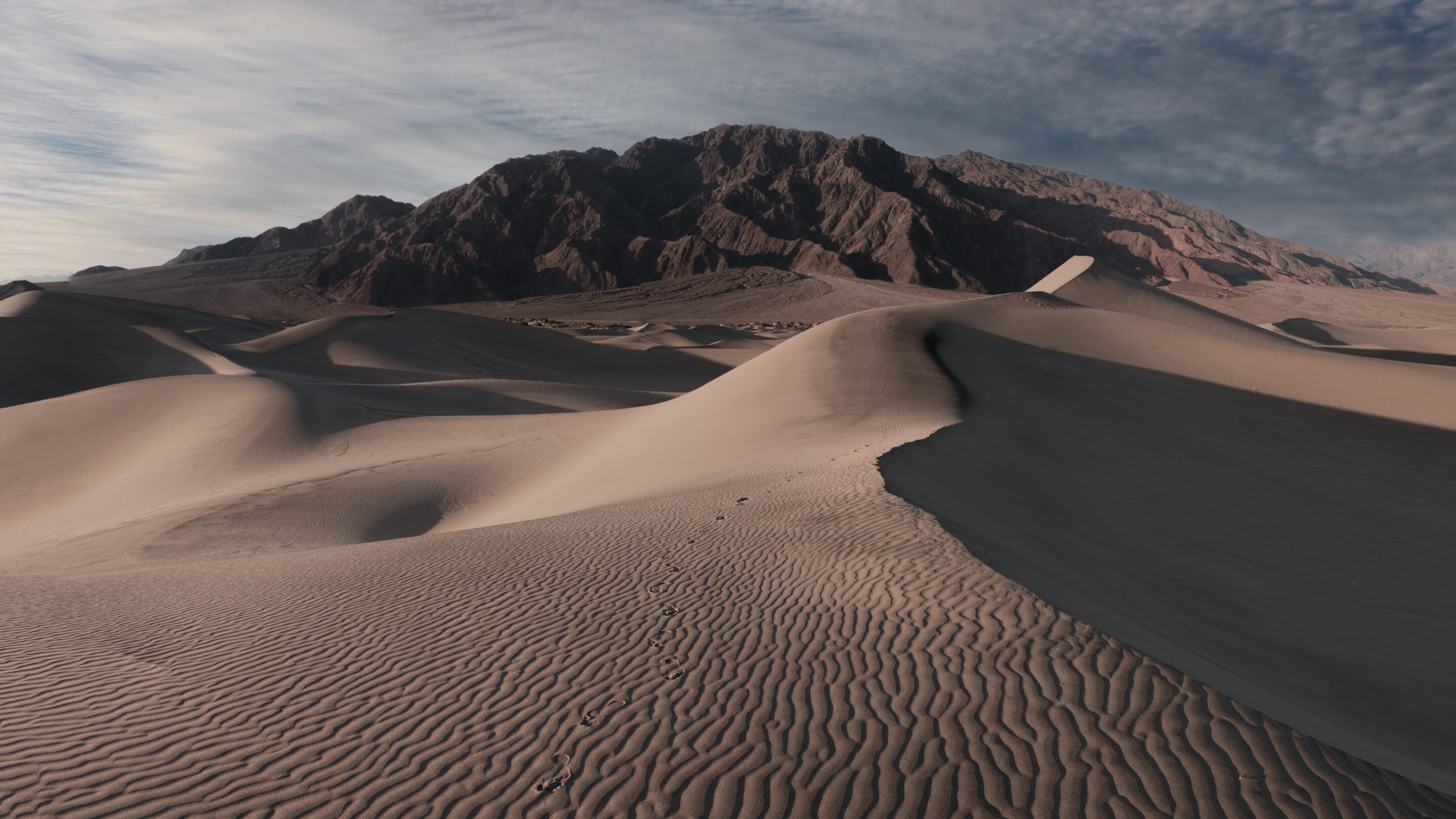 A landscape image of sand dunes with a mountain in the background