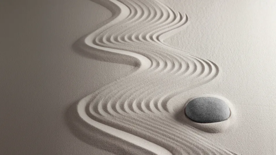 Abstract curved lines creating a wave-like pattern and a pebble in textured sand.