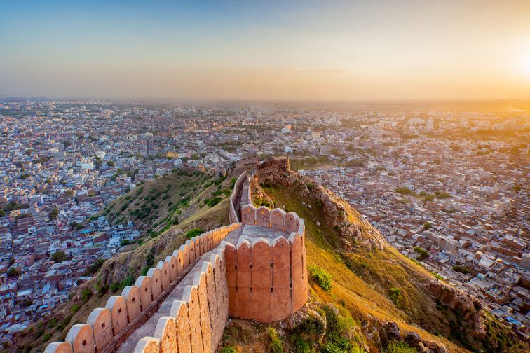 A view of historic fort wall along a hillside overlooking a populated city at sunset.