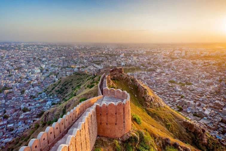 A view of historic fort wall along a hillside overlooking a populated city at sunset.