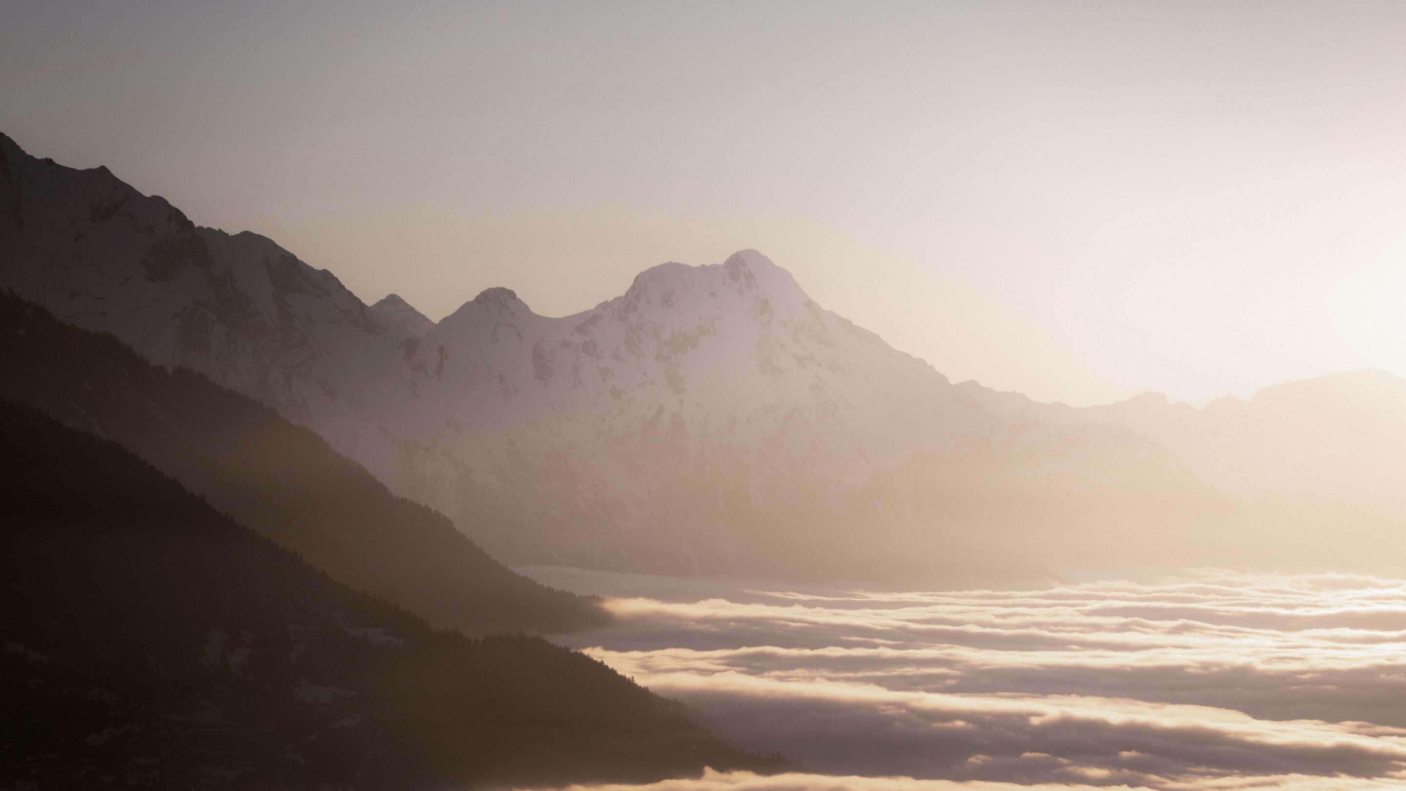 Snow-capped mountains rising above a blanket of clouds at sunrise.