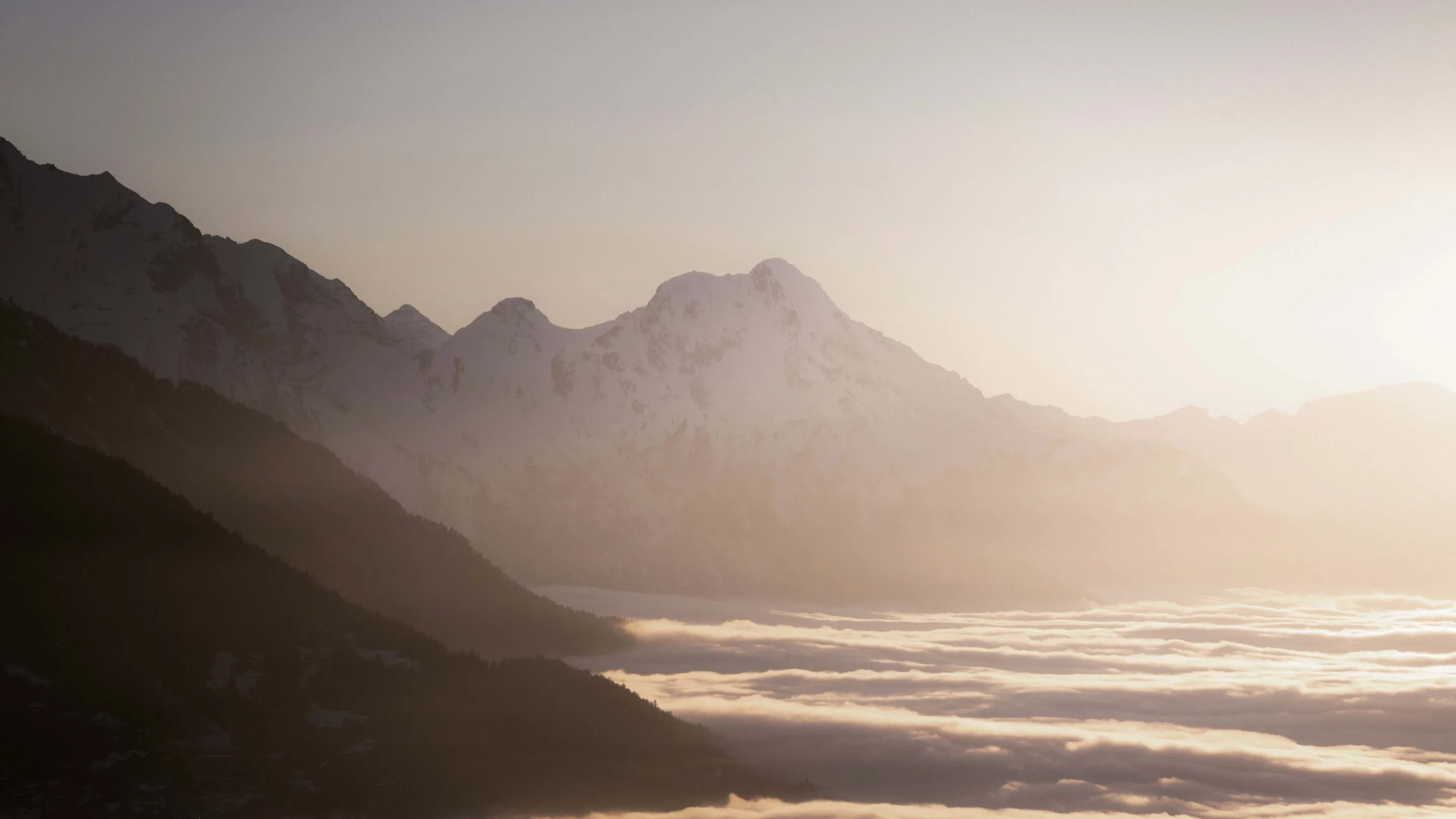 Snow-capped mountains rising above a blanket of clouds at sunrise.