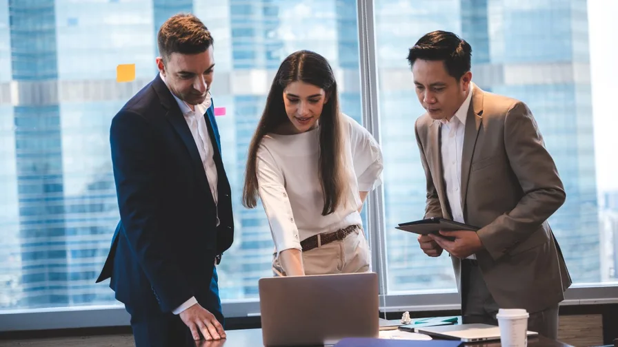 trio of business people in a discussion while standing around a laptop