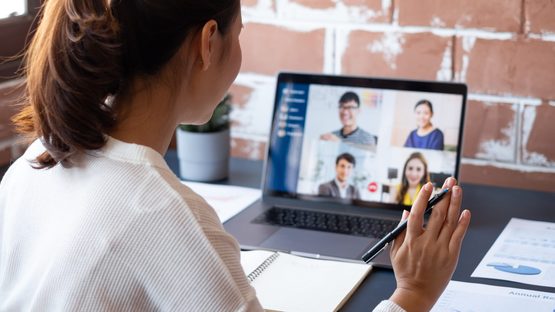 Young woman waving at screen of people in virtual meeting
