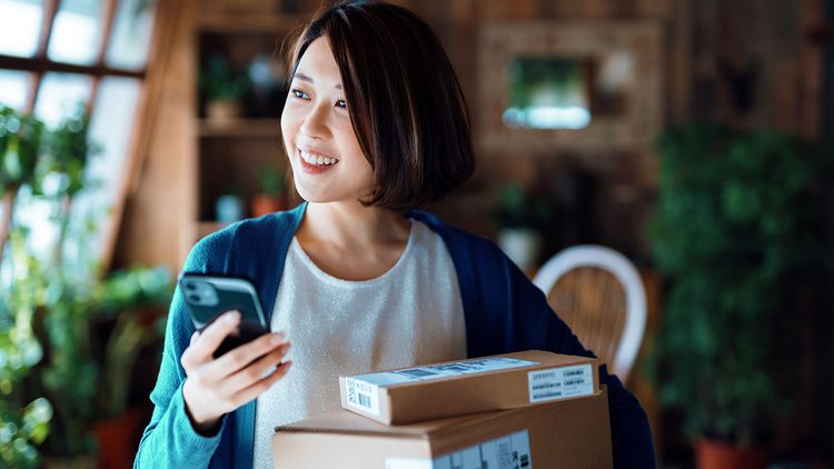 A smiling woman holds packages and her mobile phone.