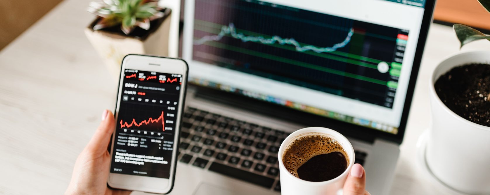 A person with phone, laptop and coffee monitoring the market