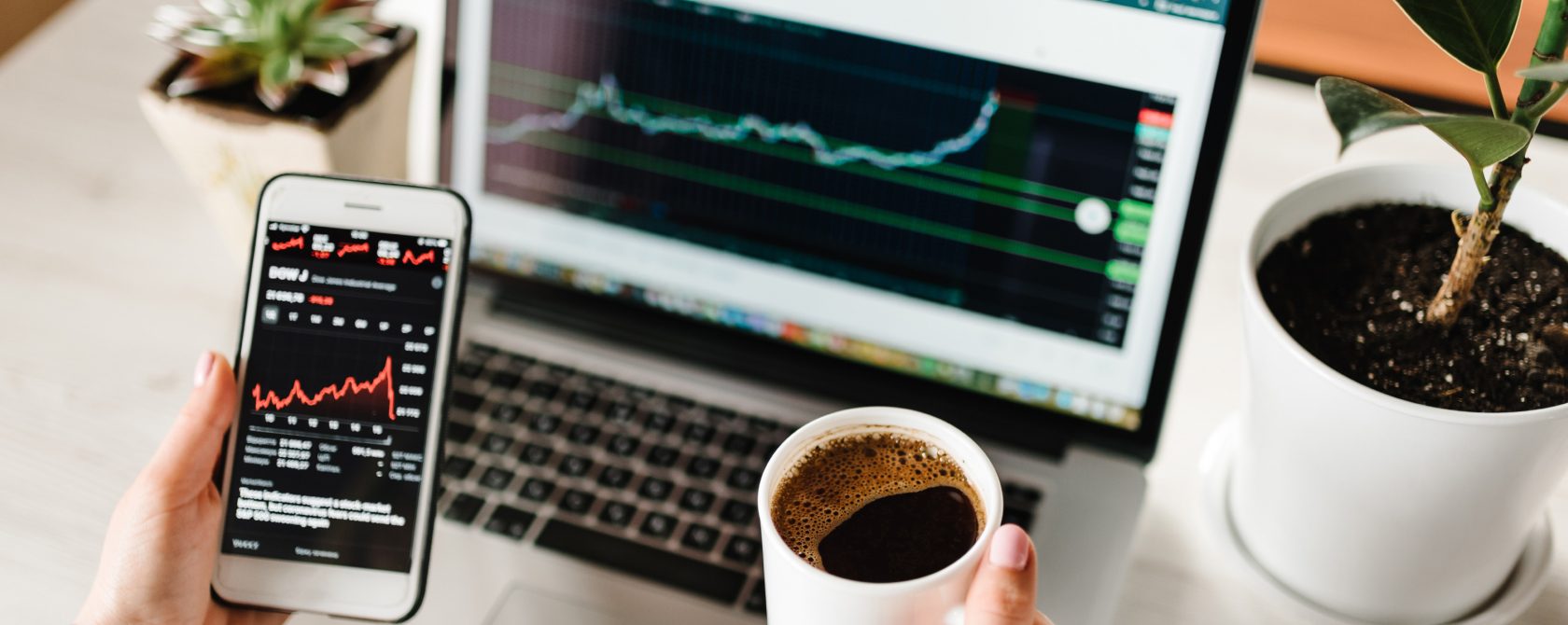 A person with phone, laptop and coffee monitoring the market