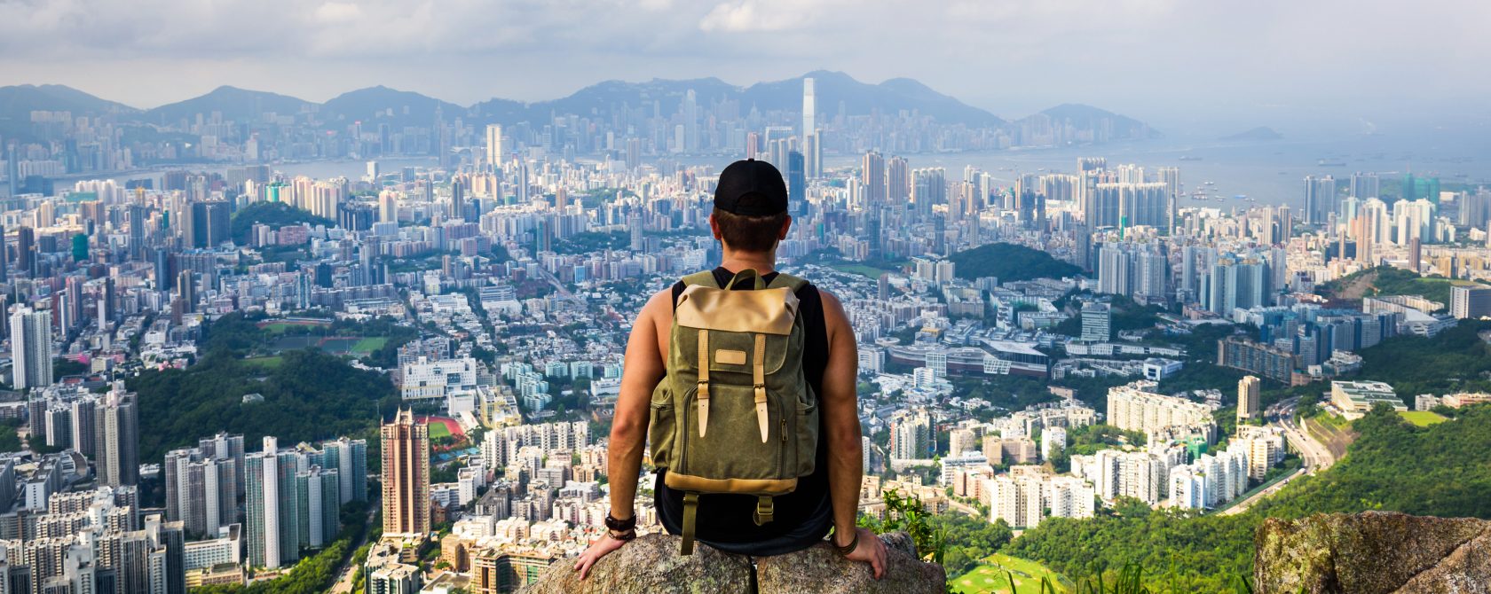 A hiker, sitting at the top of a mountain, overlooking the city.