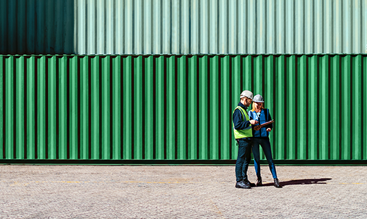 Two colleagues look at data on a tablet computer in a shipping yard as part of efforts to prevent sanctions evasion.